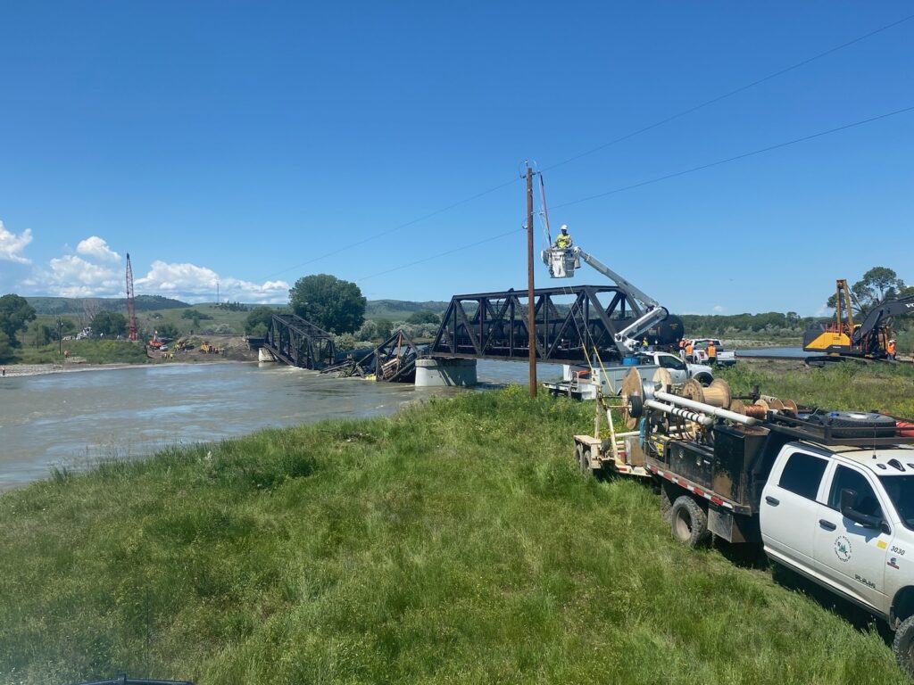 Trucks and crew working near site of bridge collapse with train cars in river